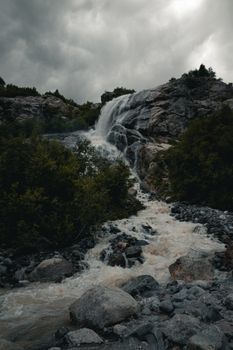 Capture of a powerful waterfall amidst rocks and lush greenery under overcast skies.