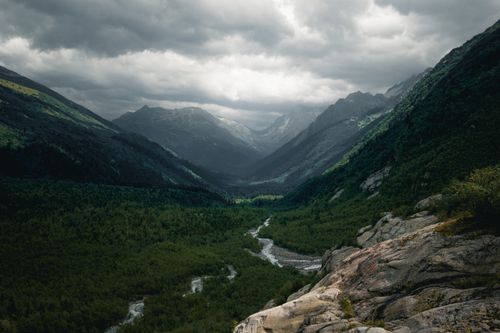 Free Stunning view of lush green mountains and a winding river under a dramatic cloudy sky. Stock Photo