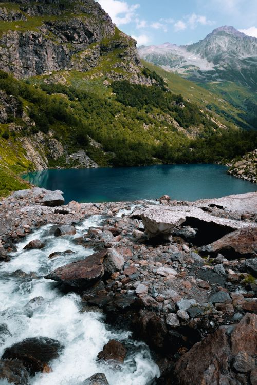 Free A picturesque mountain lake with a waterfall surrounded by lush greenery, capturing nature's beauty. Stock Photo
