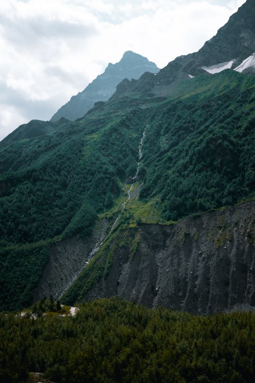 Free Capture of a lush green mountain landscape with a cascading waterfall under a cloudy sky. Stock Photo