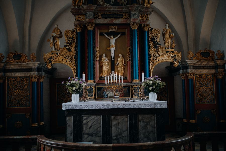 Candles and white floral arrangements near a softly lit church altar