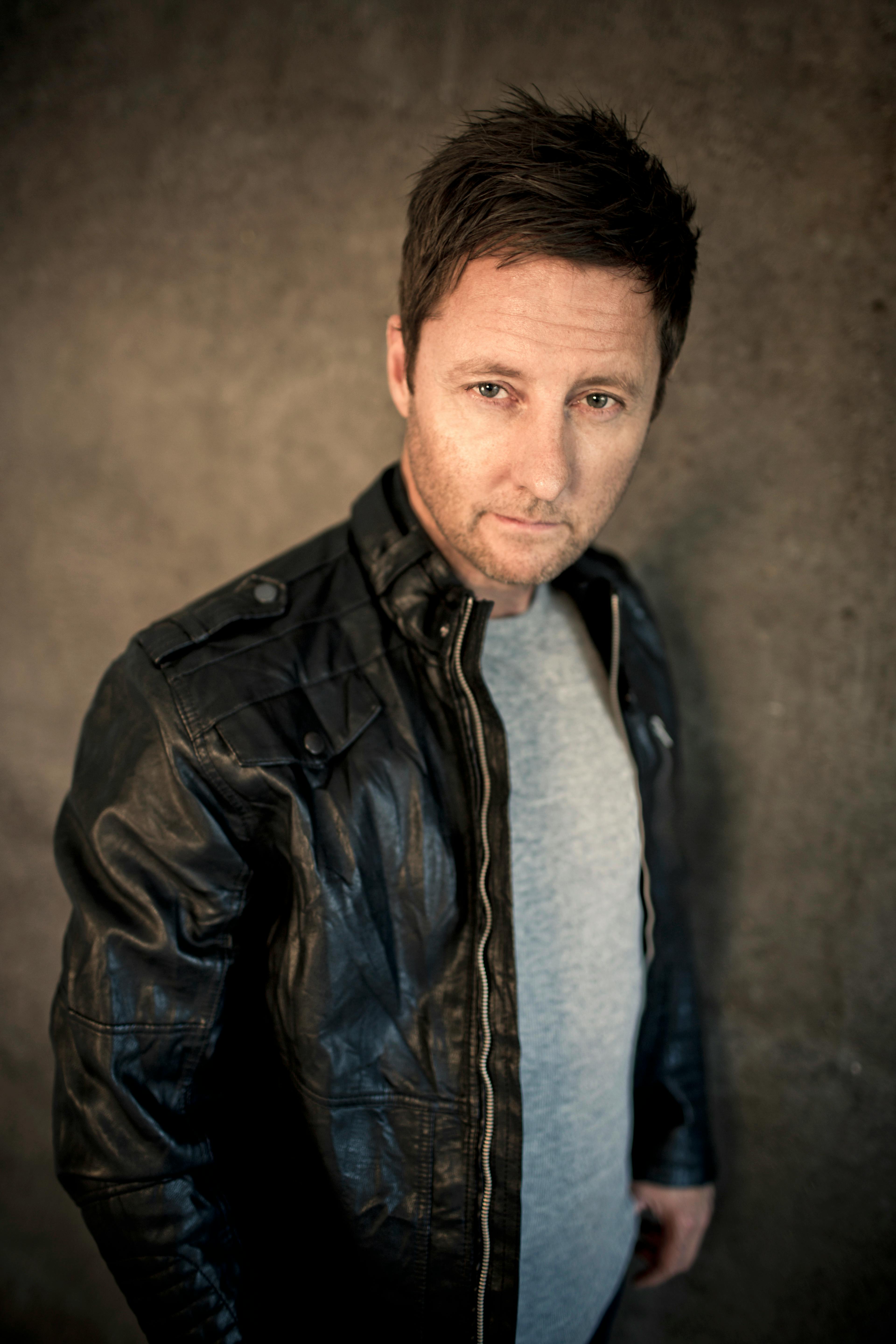 A focused portrait of a man in a leather jacket against a textured background, exuding a serious and confident demeanor.