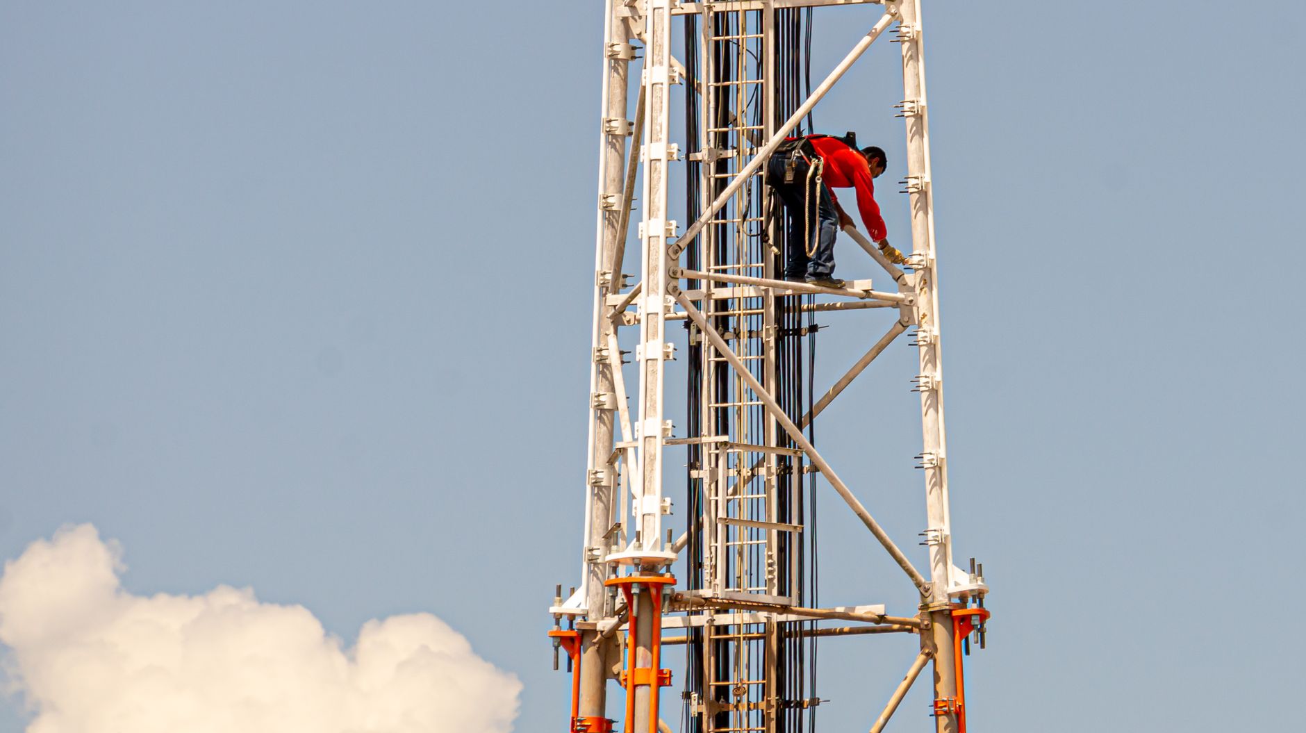 A construction worker climbing a tall communication tower against a clear blue sky in Brazil.