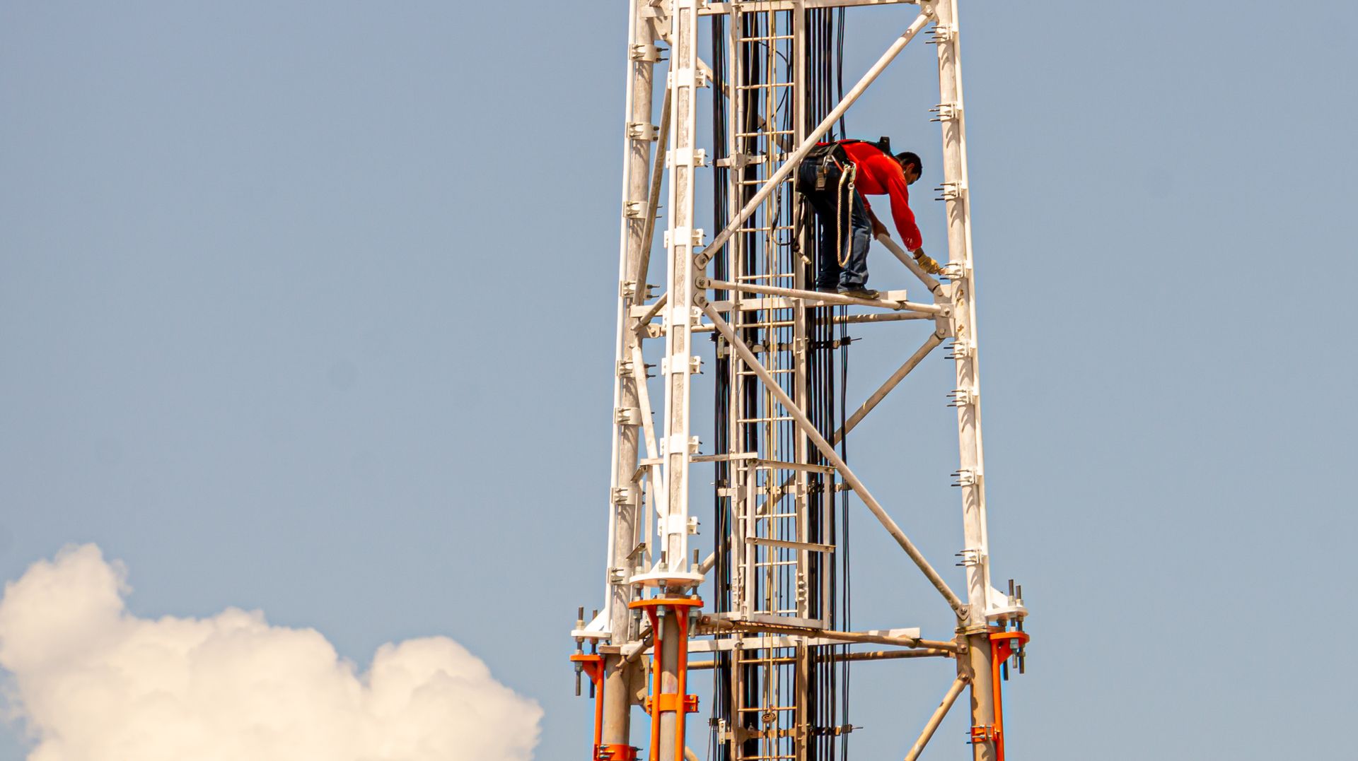 A construction worker climbing a tall communication tower against a clear blue sky in Brazil.