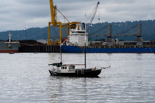 View of a Sailboat and a Cargo Ship in the Port 