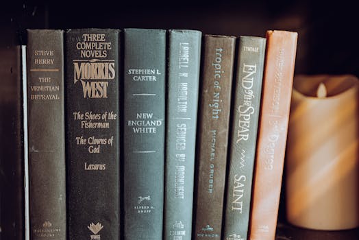 A close-up view of classic novels neatly arranged on a bookshelf with a warm-toned candle.