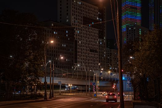 Street view of illuminated buildings and a quiet road at night in a city.
