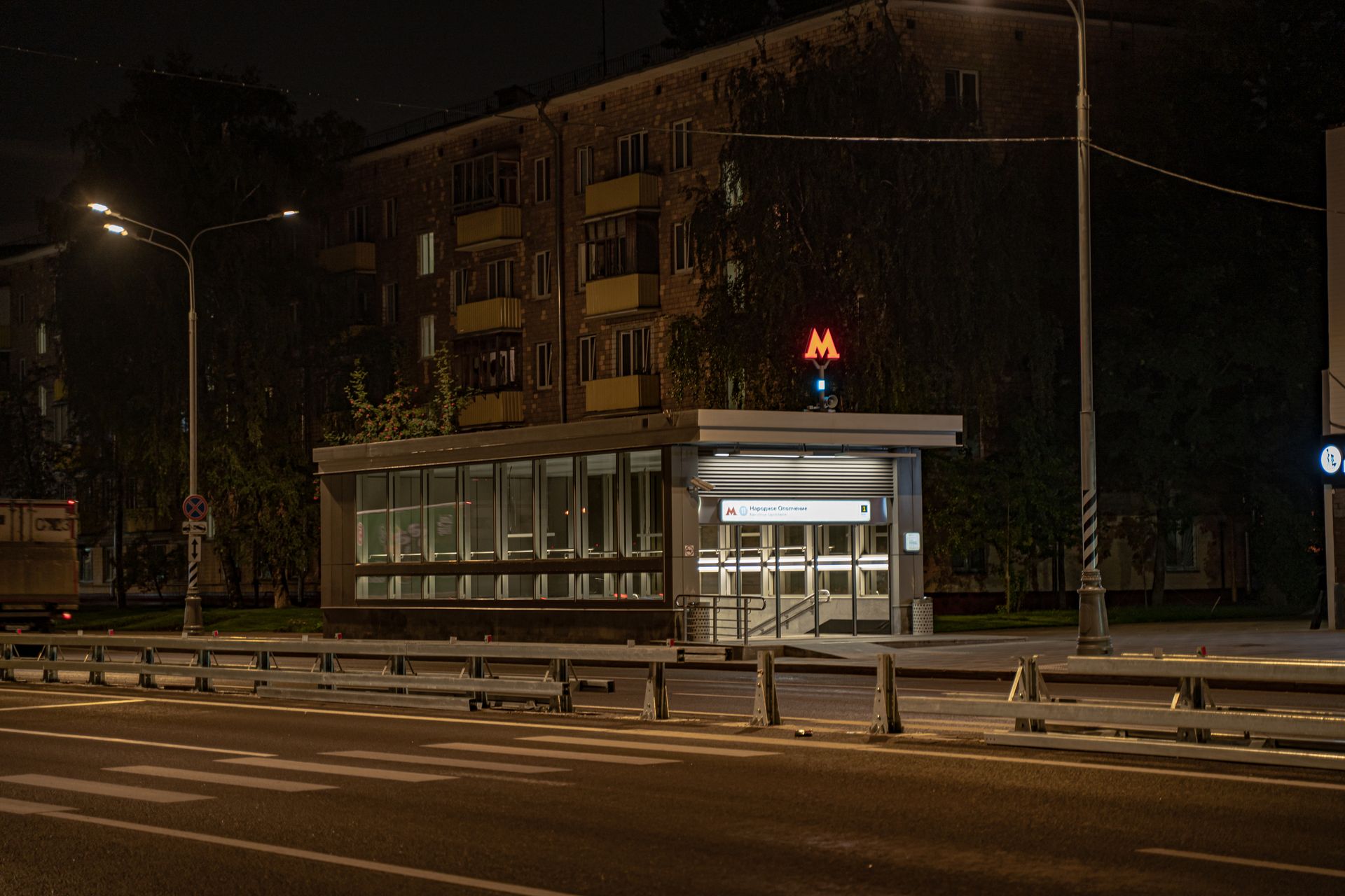 A quiet urban scene featuring a Moscow subway entrance illuminated at night.