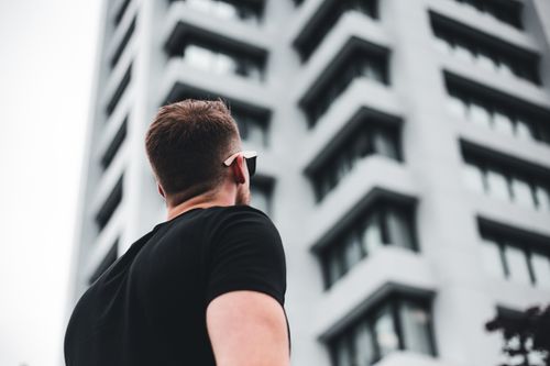 Free Back view of a man in sunglasses looking up at a tall modern building. Stock Photo