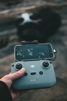 A hand holds a drone controller with a smartphone attached, showcasing a live feed.