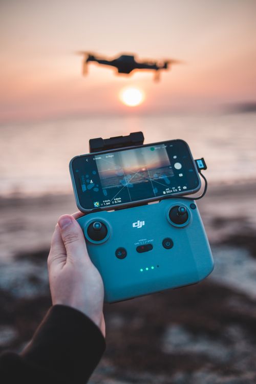 Free Close-up of hand holding drone controller while flying over the beach at sunset. Stock Photo
