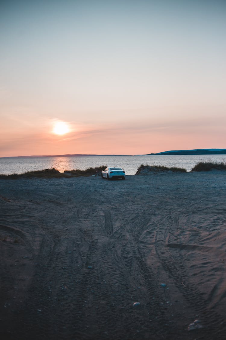 A Car Parked On The Beach During Sunset