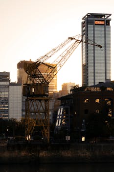 City skyline with industrial crane silhouetted against sunset, showcasing urban development.