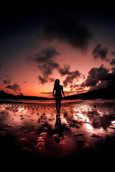 A captivating silhouette of a woman walking on the beach during a vibrant sunset.