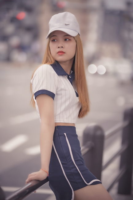 Young woman in sporty outfit leaning on a railing in cityscape with blurred background.