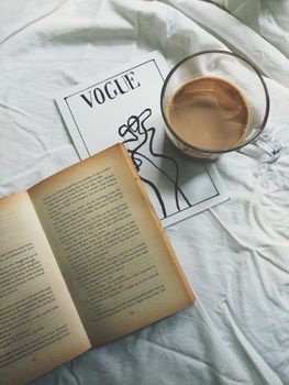 Relaxing scene with a coffee cup, open book, and magazine on a white textile surface.
