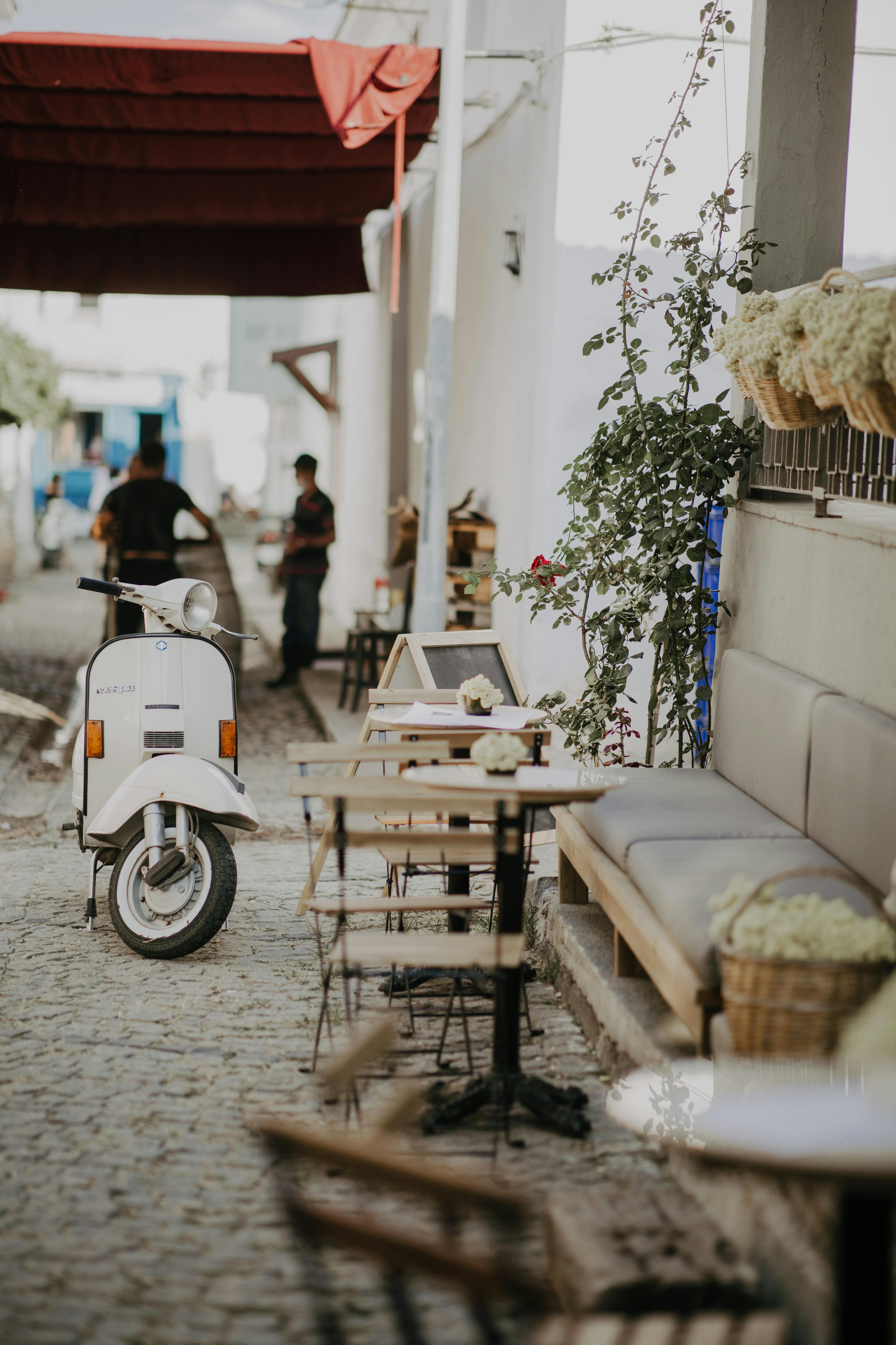 A cozy cobblestone street featuring a parked scooter and quaint outdoor café setting, inviting ambiance.
