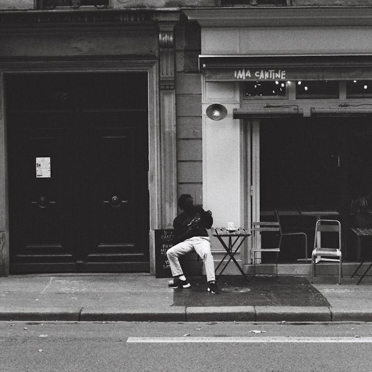 Grayscale Photo of a Man Sitting on the Street · Free Stock Photo