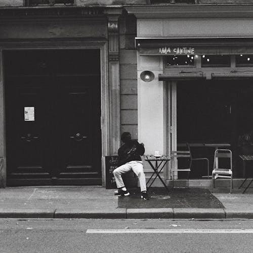 Free Grayscale Photo of a Man Sitting on the Street Stock Photo