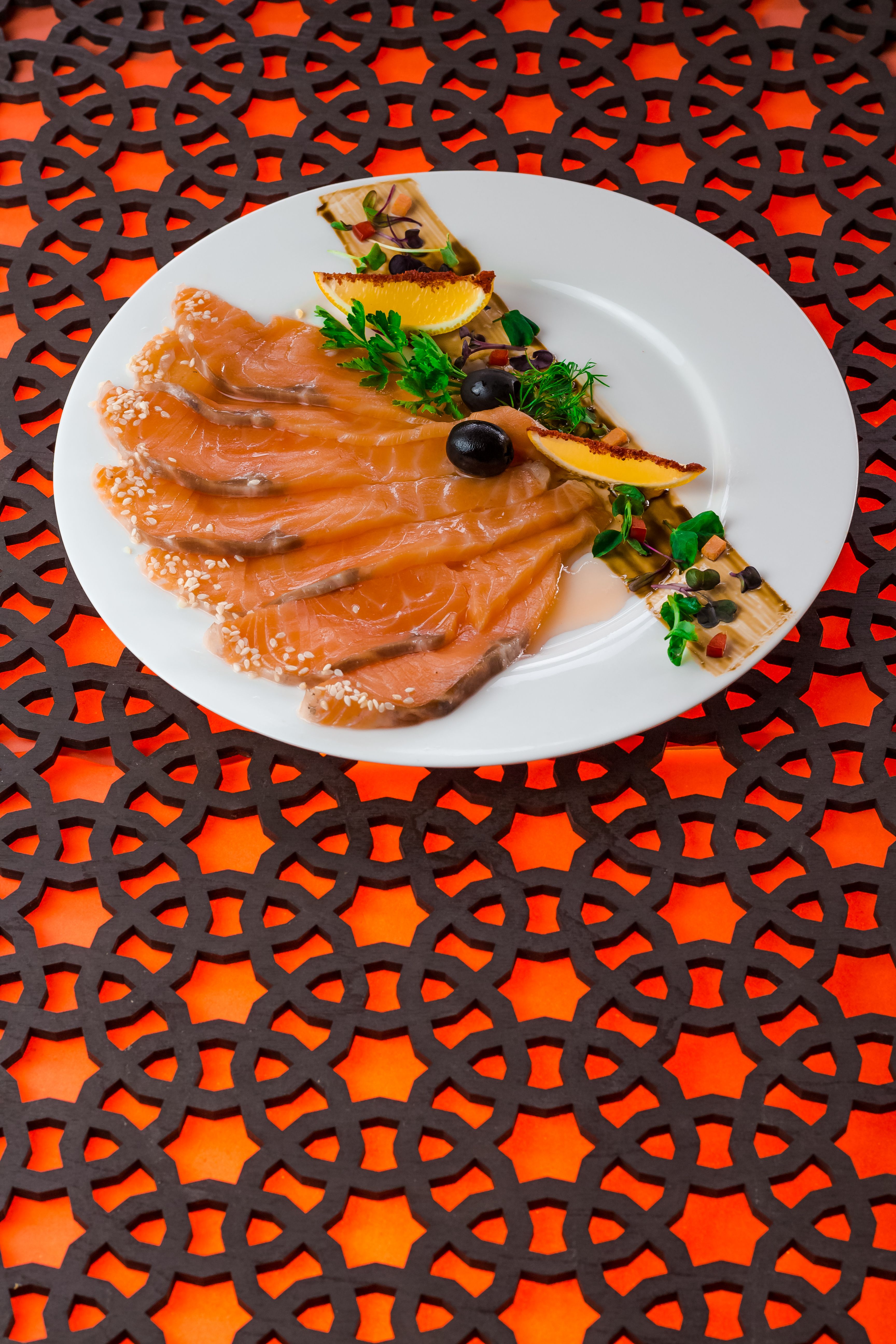 Close-up of a beautifully presented plate of smoked salmon with garnishes on a decorative table.