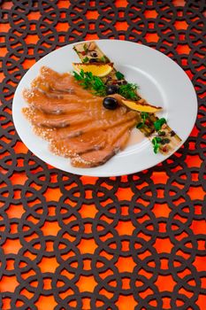 Close-up of a beautifully presented plate of smoked salmon with garnishes on a decorative table.