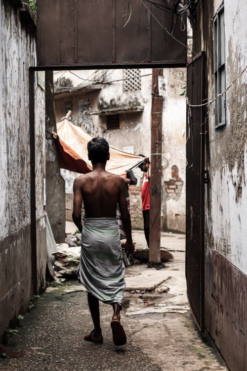 Free Back view of a shirtless man walking through a narrow alley in Dhaka, Bangladesh. Stock Photo