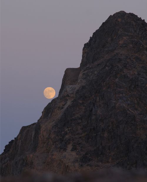 Free The moon rises above a rugged mountain, creating a serene twilight scene. Stock Photo