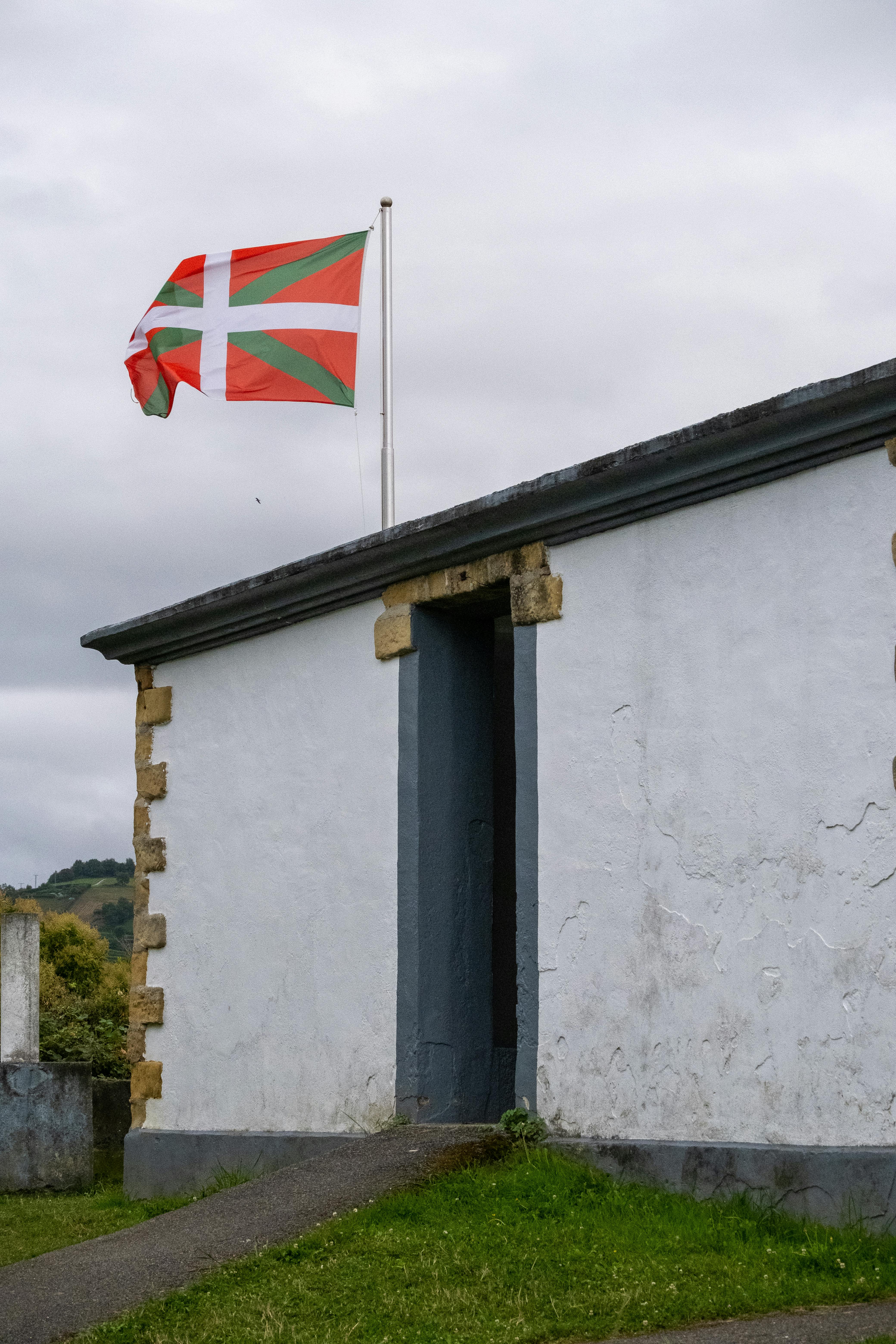 The Basque flag flies atop a traditional building with a concrete structure.