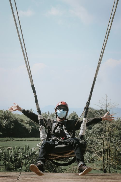 Free Man with helmet and mask swinging outdoors amidst lush greenery. Stock Photo