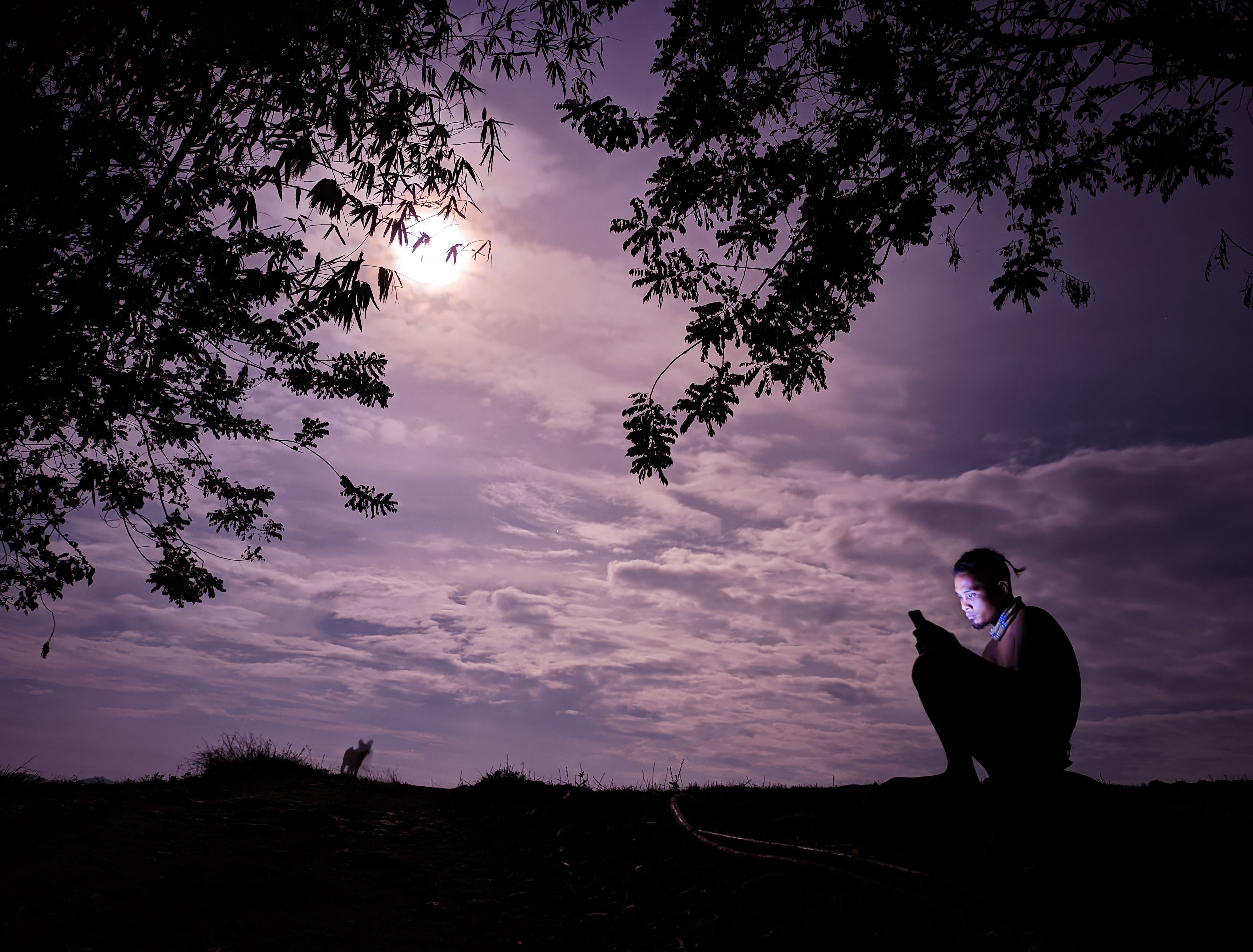 silhouette of a person sitting on a hill at sunset, hands folded in prayer or meditation, phone lying on the ground nearby