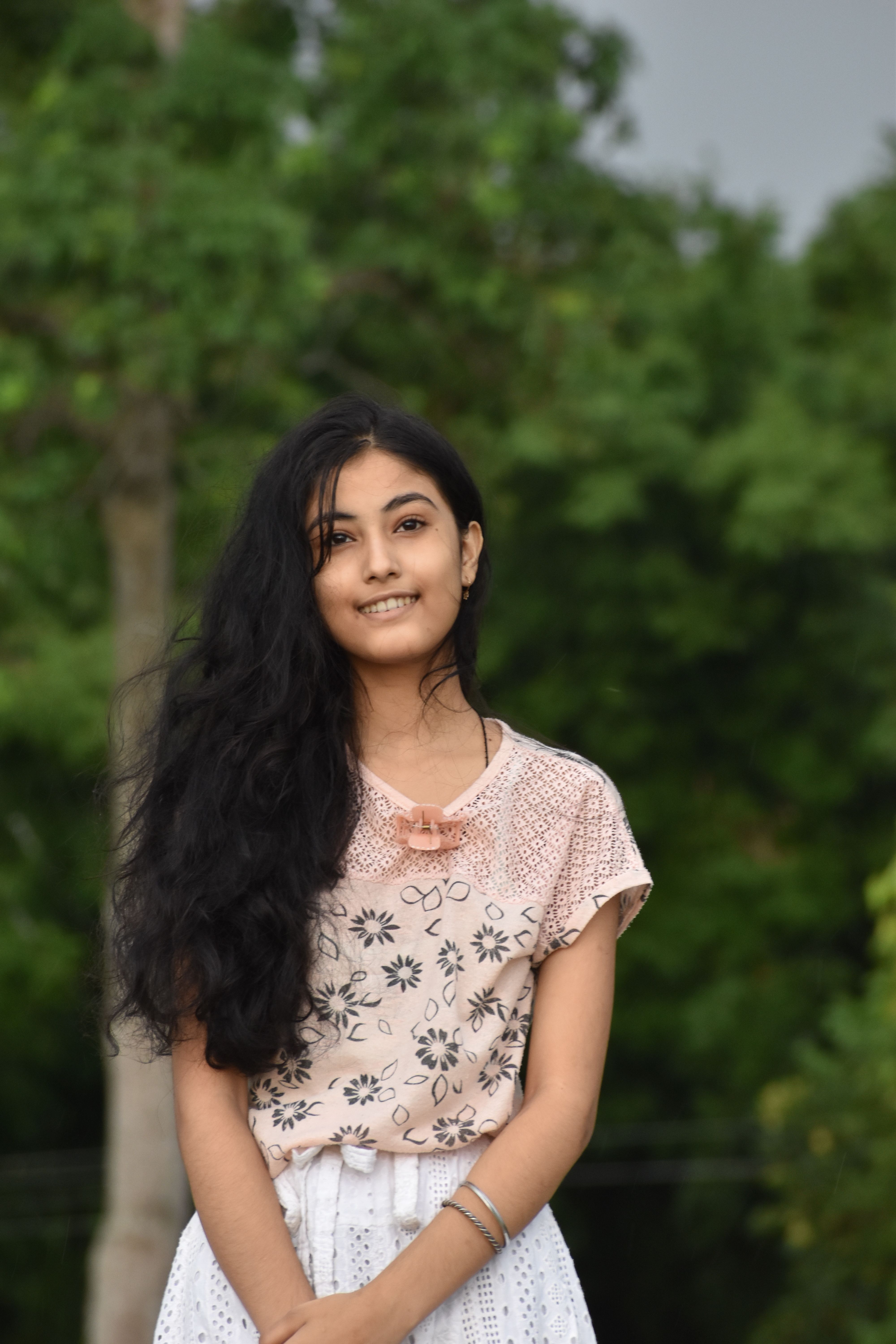 Portrait of a smiling woman wearing a floral top, enjoying nature during the day.