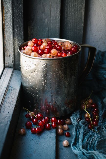 Close-up of mixed berries in a damp metal mug by a rustic windowsill.