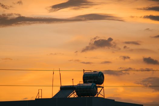 Sunset silhouette of an industrial rooftop against orange sky with tanks and antennas.