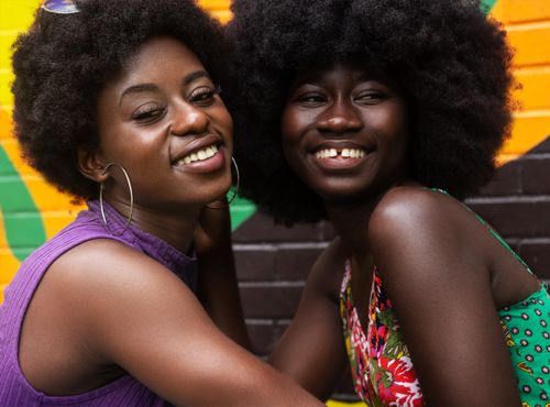 Free Two smiling women with afro hairstyles embracing against a colorful backdrop, showcasing friendship and happiness. Stock Photo