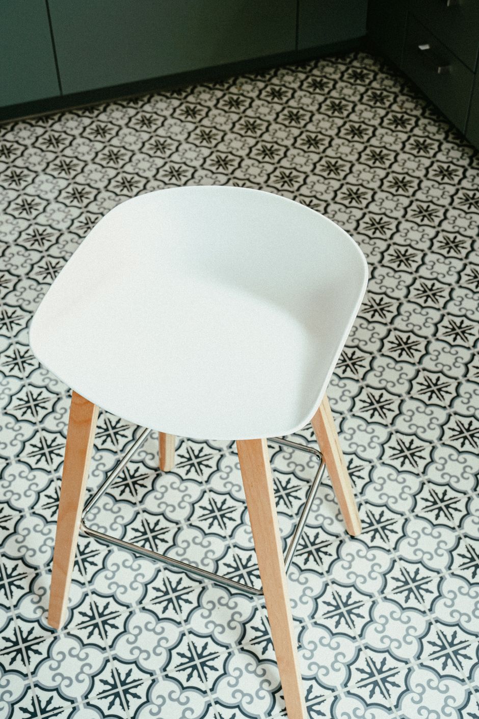 A sleek white stool sits on a stylish black and white patterned tile floor.