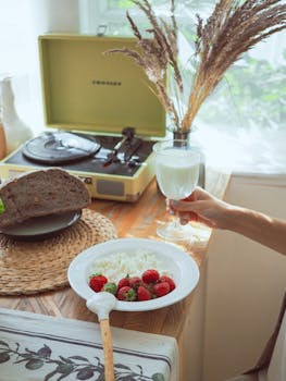 Cozy breakfast with strawberries, yogurt, and a vintage record player in a warm setting.