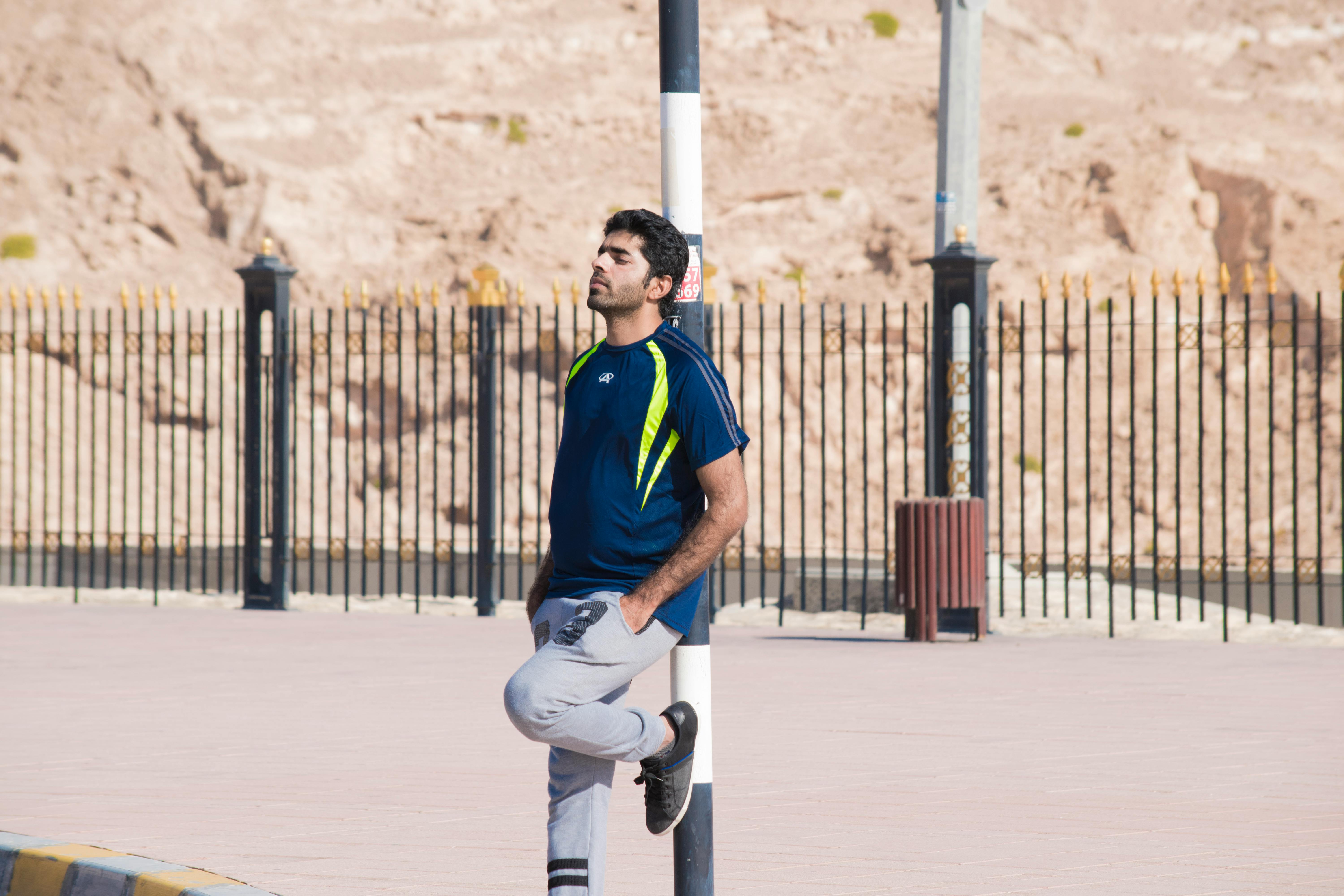 一名穿着运动服的男子靠在城市户外环境中的杆子上