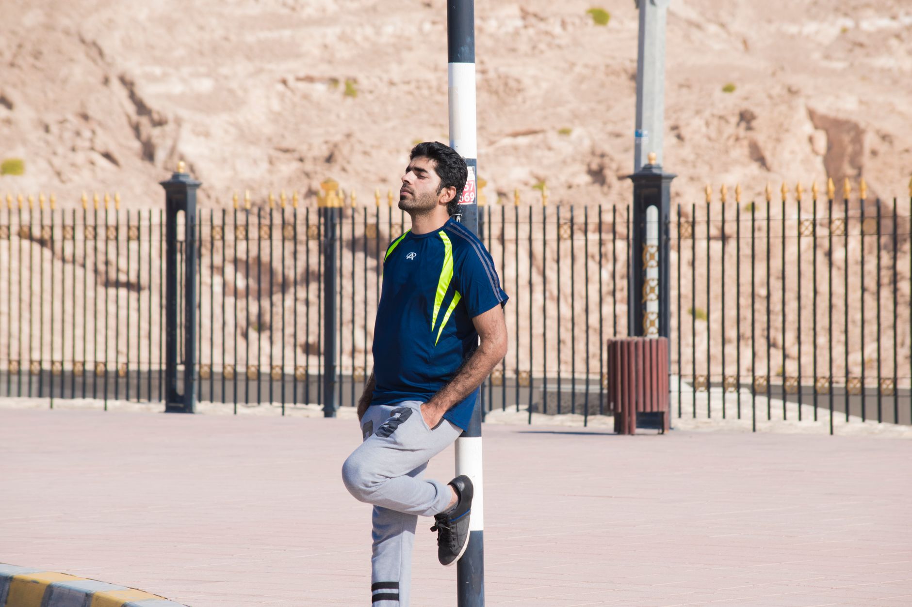 A man in sportswear leans against a pole in an urban outdoor setting.