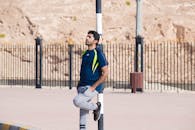 一名穿着运动服的男子靠在城市户外环境中的杆子上