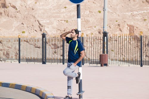 Man Wearing Blue Crew-neck Shirt Leaning on Street Post