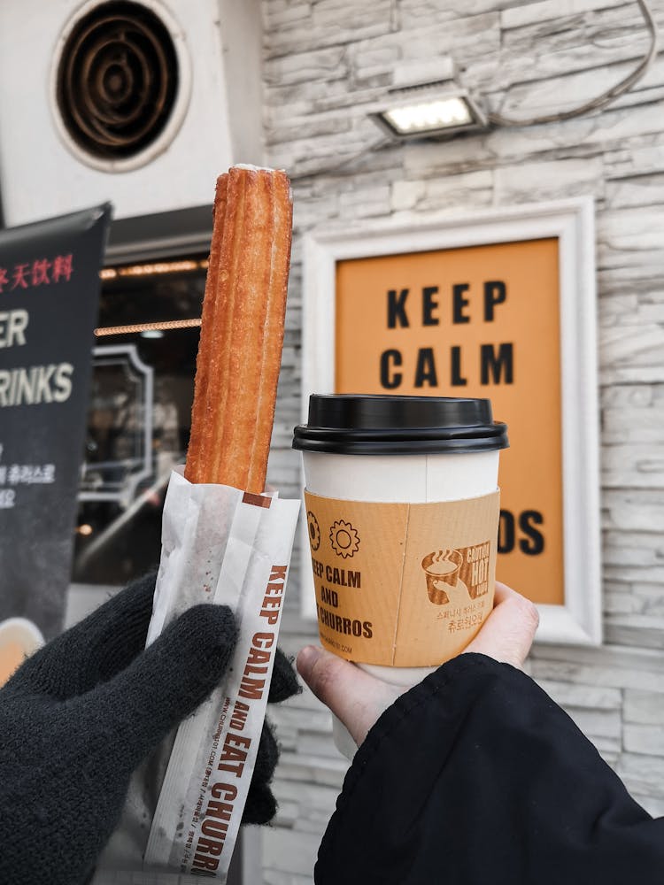 Close-up Of Holding A Churro And Cup Of Coffee