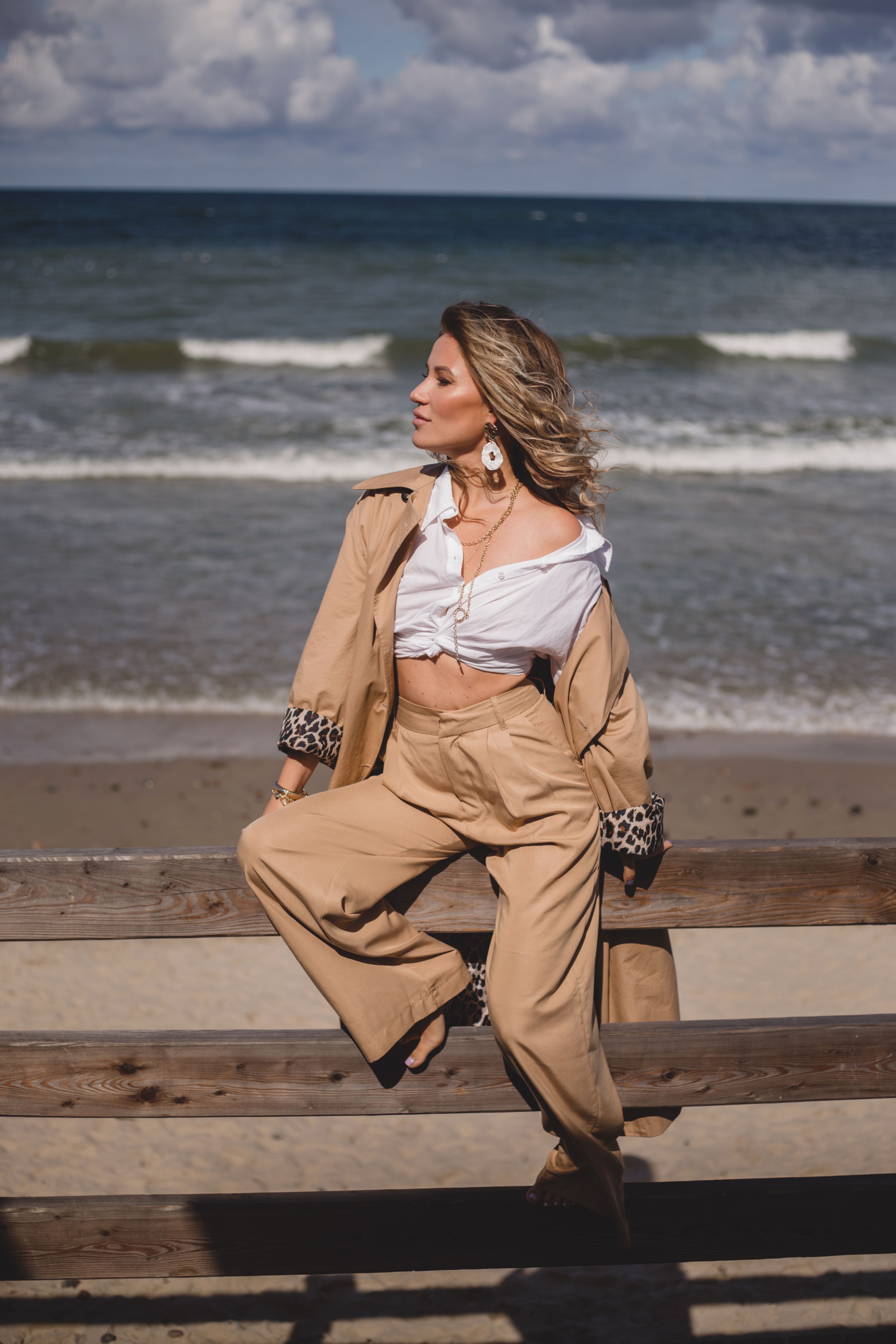 Elegant woman poses at the beach on a breezy day, showcasing modern fashion.