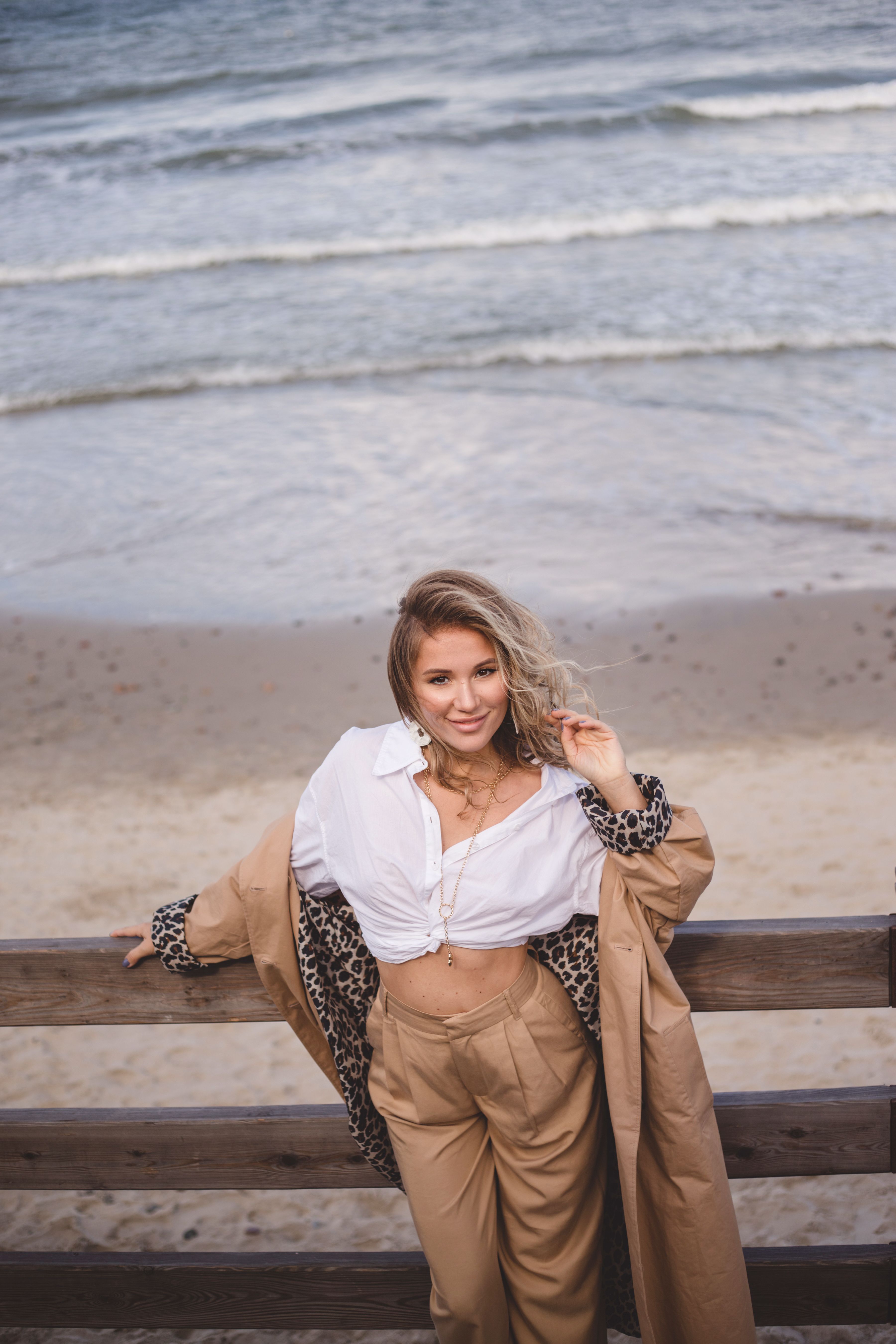 Fashionable woman standing by the seaside, showcasing a trendy outfit with waves in the background.
