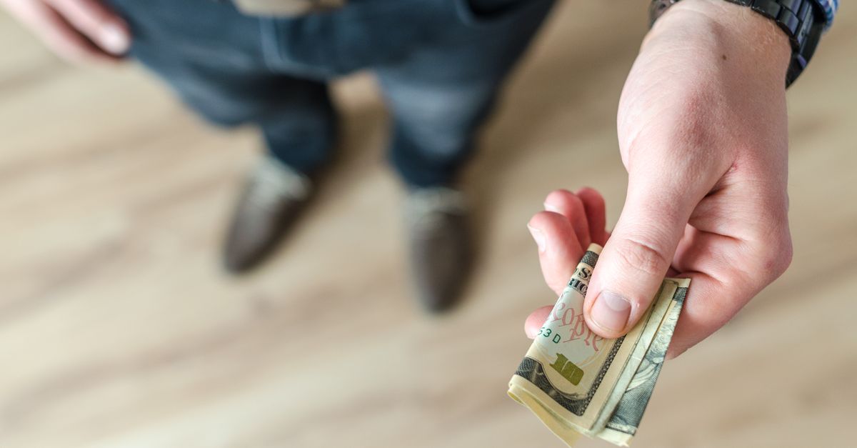 A close-up of a hand placing cash into an offering basket, with soft lighting and a focus on intention