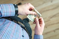 特写镜头中，一名穿着休闲装的男子手里拿着美元