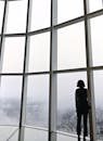 一名女子站在现代化高层建筑的大窗旁，俯瞰着首尔的天际线