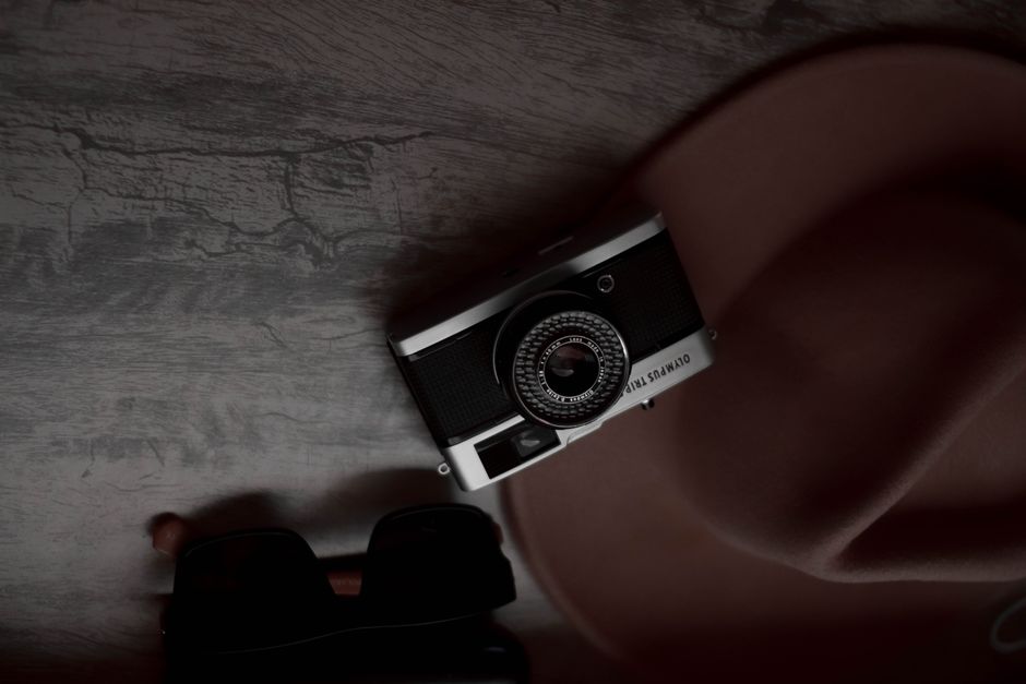 A stylish flat lay featuring a vintage camera, fedora hat, and sunglasses on textured surface.