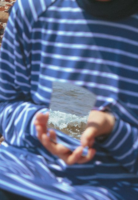 A person's reflection in a mirror showing ocean waves, with hands holding it.