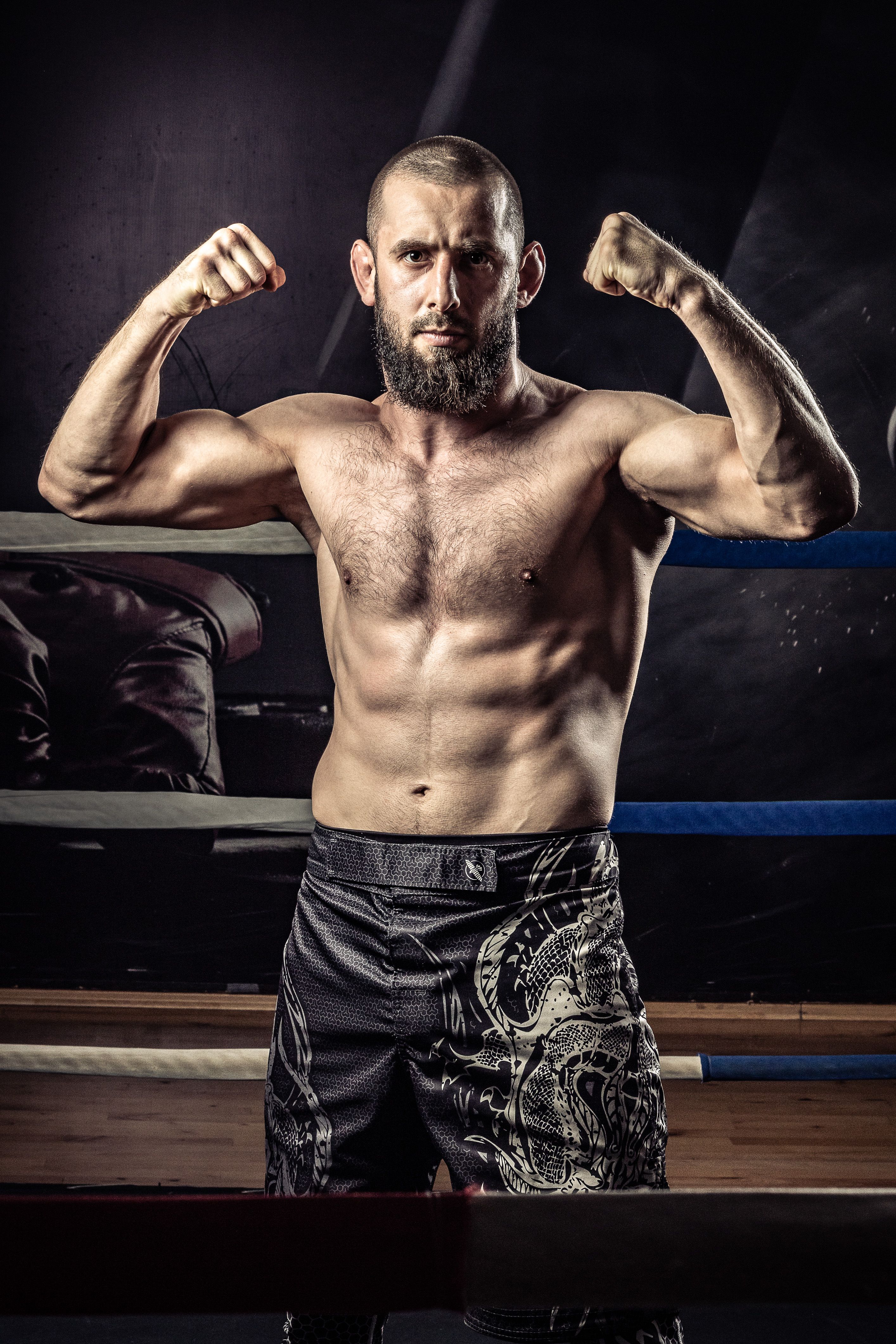 Bearded muscular man flexing in a boxing ring, showcasing strength and fitness.