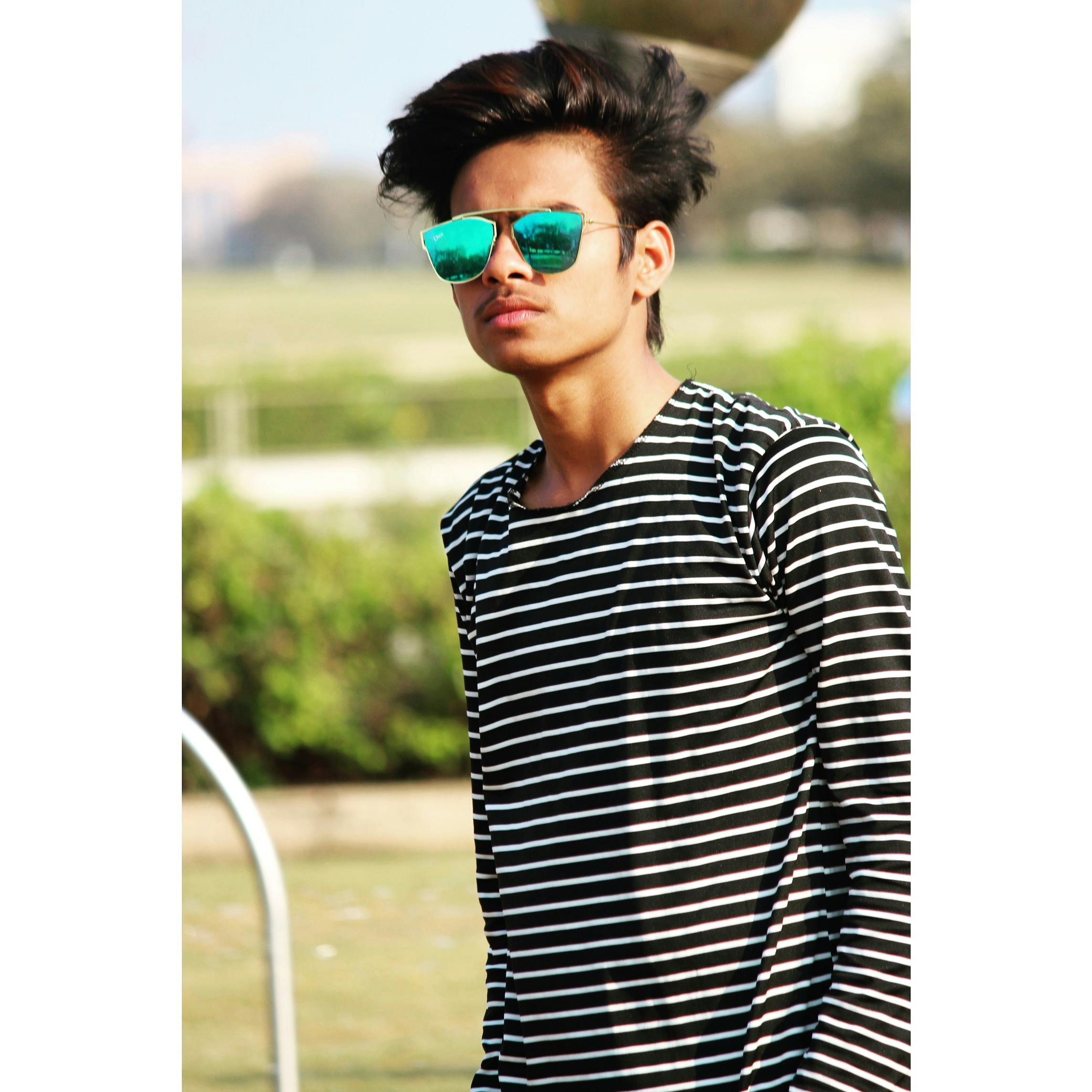 一名年轻人戴着墨镜、穿着条纹衬衫，在户外公园自信地摆姿势